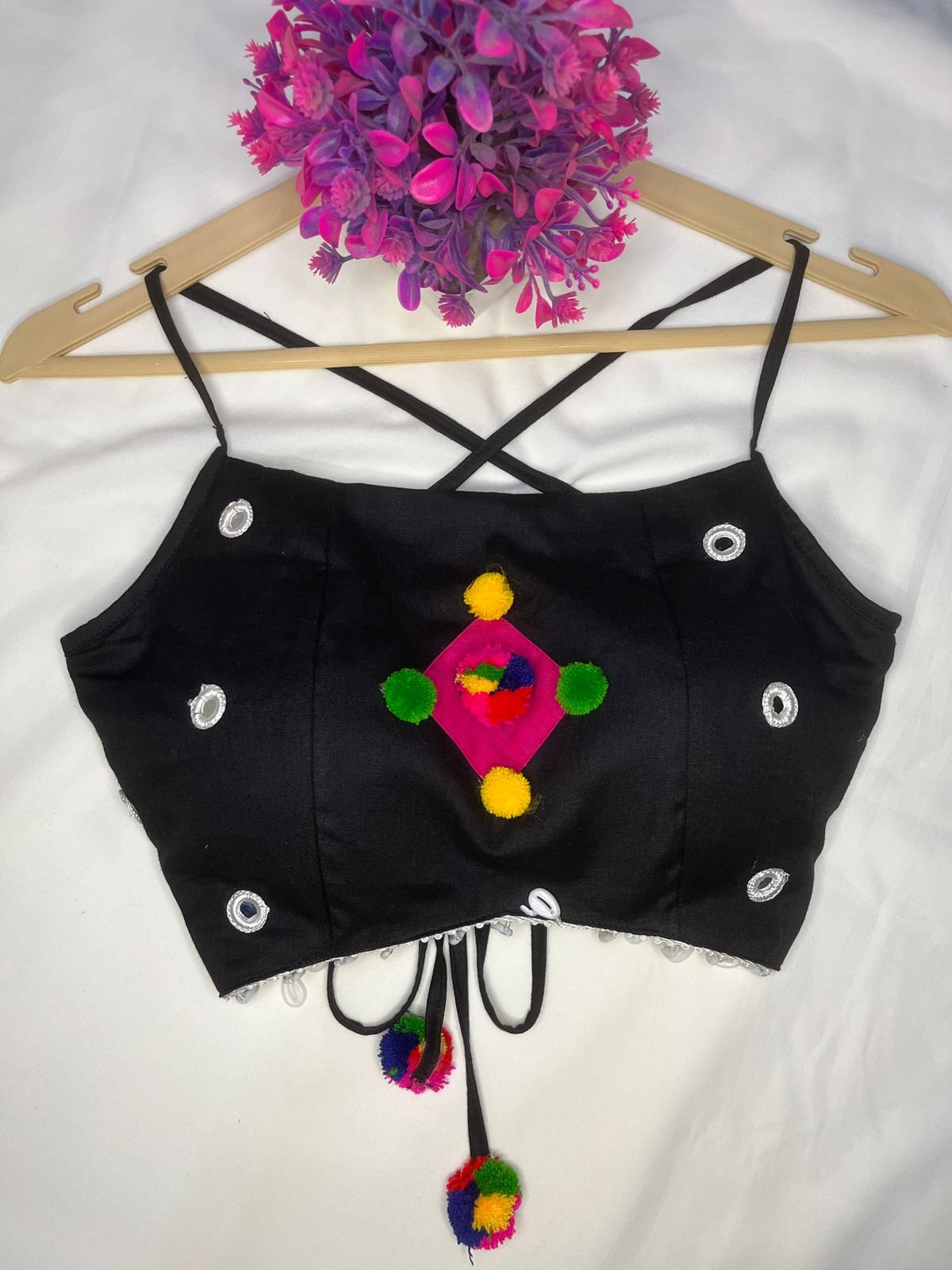 This black cotton crop top blouse, decorated with multicolor pompoms and mirror work, will add a fun, vibrant touch to your festive outfits.